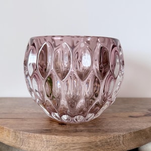 May include: A translucent, dusty rose-colored glass bowl featuring a repeating, molded honeycomb or diamond-shaped pattern across its exterior surface. The bowl has a rounded, bulbous shape with a wide opening and a smooth, clear glass rim.