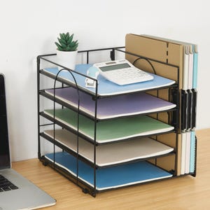 May include: A black metal desk organizer with four horizontal shelves and a vertical side compartment. The shelves hold stacked notebooks in blue, purple, green, and white. A white calculator and a small potted succulent sit on the top shelf.