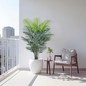 Könnte beinhalten: Eine hohe künstliche Palme mit leuchtend grünen Wedeln in einem großen, glatten, weißen, abgerundeten Pflanzgefäß. Neben der Pflanze steht ein kleiner Beistelltisch aus Holz mit zwei winzigen Topfpflanzen sowie ein Holzstuhl mit grauem Kissen.