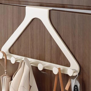 Op de afbeelding: Een crèmekleurig deurhaakrek in de vorm van een grote kledinghanger. Het rek is voorzien van vijf cilindrische haken aan de onderkant, die ruimte bieden voor het ophangen van voorwerpen zoals een beige jas, een paraplu en een tas.