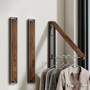 May include: Three wall-mounted garment racks featuring a dark wood grain panel framed in matte grey metal. Two racks are in a closed, vertical position, while the third is extended outward, supporting a horizontal rod with four metal clothes hangers.
