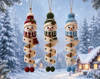 Könnte beinhalten: Drei hängende Häkel-Schneemann-Ornamente mit Strickmützen und Schals in Rot, Grün und Blau. Jeder Schneemann hat einen langen, spiralförmigen, cremefarbenen Körper, der mit gestickten Schneeflocken, kleinen Perlen und zwei passenden Bommeln verziert ist.