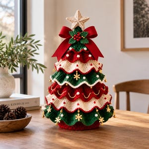 Pode incluir: Uma decoração de árvore de Natal em crochê com camadas onduladas alternadas em fio verde-escuro e creme. A árvore é rematada com uma estrela de crochê bege, um laço vermelho e bagas de azevinho. É decorada com pequenos flocos de neve dourados e contas brancas.