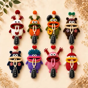 May include: Eight crocheted monster-shaped key pouches in various colors including red, orange, green, brown, blue, purple, and pink. Each pouch features two white eyes, a wide open mouth, and a loop holding a black car key fob at the bottom.