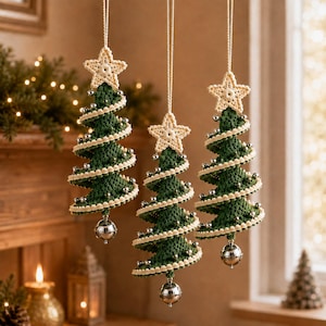 Op de afbeelding: Drie hangende kerstboomornamenten gemaakt van donkergroen haakgaren. Elke boom heeft een spiraalvormig ontwerp afgewerkt met crèmekleurige gehaakte randen, kleine zilveren kralen, een crèmekleurige gehaakte ster aan de top en een zilveren bel onderaan.