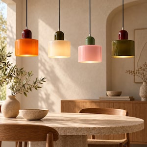 Puede incluir: Cuatro lámparas colgantes cilíndricas cuelgan de cables negros. La primera tiene una pantalla naranja con una parte superior roja oscura, la segunda una pantalla crema con una parte superior verde oscura, la tercera una pantalla rosa con una parte superior verde y la cuarta una pantalla verde oscura con una parte superior roja.