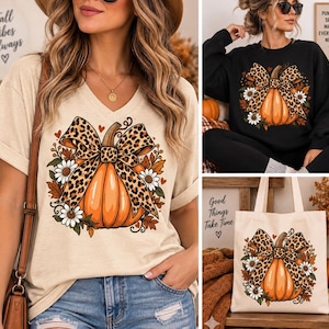 Puede incluir: Una camiseta beige con cuello en V, una sudadera negra con cuello redondo y una bolsa de tela beige, cada una con un estampado gráfico de una calabaza naranja adornada con un gran lazo de estampado de leopardo, margaritas blancas y hojas otoñales.