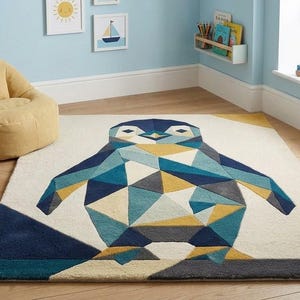 May include: A rectangular area rug featuring a large, geometric penguin design composed of triangular shapes in shades of navy blue, teal, mustard yellow, and grey on a cream-colored background, with a dark navy border along the bottom edge.