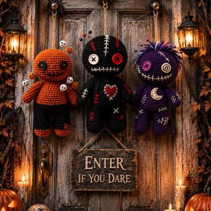 May include: Three crocheted dolls hanging on a wooden door with a sign that reads ENTER IF YOU DARE. The dolls are orange, black, and purple, featuring button eyes, stitched mouths, and various decorative pins. Two jack-o'-lanterns and a skull sit below.