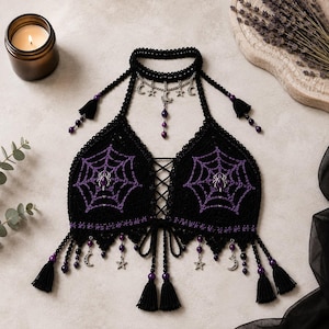May include: A black crochet halter top featuring purple spiderweb embroidery and silver spider charms. The garment includes a choker neckline with silver moon and star charms, purple bead accents, and black tassels along the bottom hem.