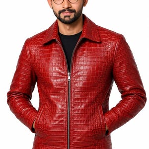 Puede incluir: Una chaqueta de color rojo brillante con un patrón texturizado de piel de cocodrilo, cuello clásico y cierre de cremallera metálica plateada en el centro. La prenda incluye dos bolsillos laterales y mangas largas, ofreciendo un ajuste estructurado.