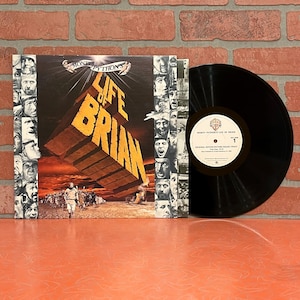 May include: A vinyl record and album cover for Monty Python's "Life of Brian." The album cover features the title in large, gold block letters with a brick-like design. The record is black with a white label.
