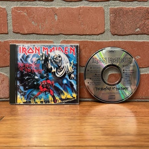 May include: An Iron Maiden The Number of the Beast music CD in a clear plastic jewel case with cover art featuring a skeletal figure and a red devil, alongside the metallic silver disc printed with track titles and the band logo in black text.