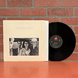 May include: A vinyl record album by Howard Jones, titled "Human's Lib." The album cover features a black and white photo of four people. The record is black with a red and white label.
