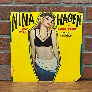 May include: A vintage vinyl record album cover for Nina Hagen, titled "New York." The album art features a woman in a black bra and jewelry, with the artist's name in large, bold letters. The background is bright yellow.