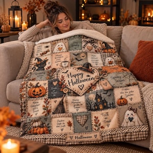 Könnte beinhalten: Eine plüschige, cremefarbene Wohndecke mit Patchwork-Design und Halloween-Motiven wie Kürbissen, Geistern, einem Spukhaus und einem Besen. Auf dem herzförmigen Aufnäher in der Mitte steht der Text Happy Halloween.
