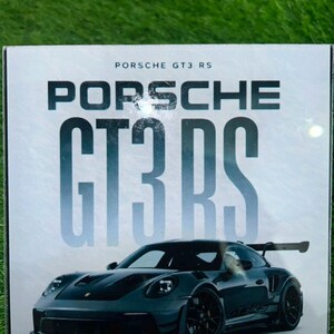 Peut inclure: Une plaque carrée présentant le texte PORSCHE GT3 RS en lettres noires grasses en haut. Sous le texte se trouve une image détaillée d'une voiture de sport Porsche GT3 RS gris foncé avec un aileron arrière, des roues noires et un design aérodynamique.