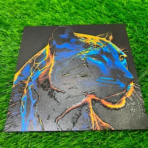May include: A square black plaque featuring a relief illustration of a panther head in profile. The panther is accented with vibrant neon blue and orange lightning-like patterns that trace its features, ears, and whiskers against the dark surface.