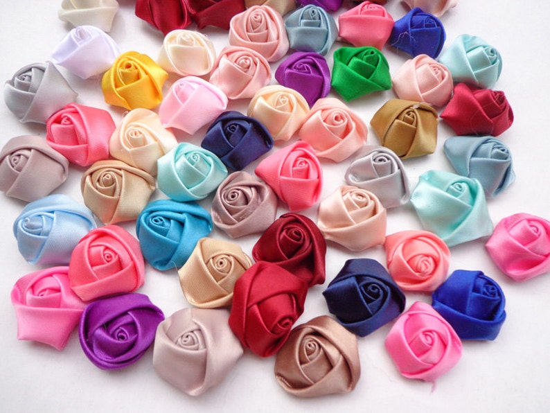 May include: Assortment of small, handmade satin fabric roses in various colors, including pink, blue, purple, red, white, and green. The roses are approximately 1 inch in diameter.