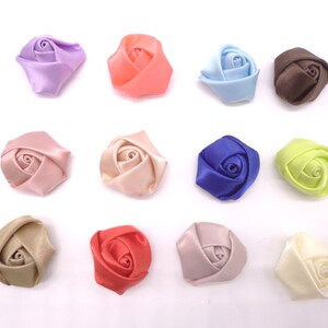 May include: Twelve small satin fabric rose flower embellishments in various colors, including pink, peach, lavender, blue, brown, green, red, and cream.