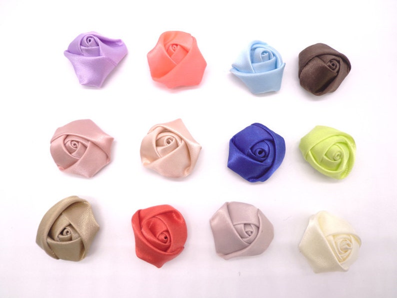 May include: Twelve small satin fabric rose flower embellishments in various colors, including pink, peach, lavender, blue, brown, green, red, and cream.