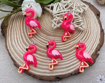 May include: Five pink flamingo charms with black eyes and gold accents. The charms are made of resin and have a hole at the top for attaching to jewelry or other crafts.