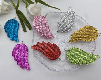 May include: Six glitter angel wings in different colors: pink, blue, silver, gold, red, and green. Each wing has a hole at the top for hanging or attaching.