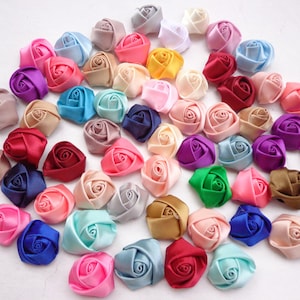 May include: Assortment of colorful satin ribbon roses in various shades of pink, blue, red, green, purple, brown, and yellow. The roses are approximately 1 inch in diameter.