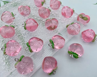 May include: A collection of pink, translucent strawberry charms with green leaves and silver-colored loops. The charms are filled with glitter and have a realistic shape, perfect for jewelry making or crafting projects.