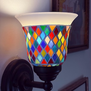 May include: A wall-mounted sconce light featuring a flared, frosted glass rim and a shade composed of multi-colored, diamond-shaped glass tiles in red, orange, yellow, green, and blue. The fixture has a matte black metal base and arm.