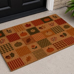 May include: A rectangular coir doormat featuring a patchwork design of autumn-themed squares. The pattern includes orange pumpkins, brown acorns, red and brown fall leaves, small flowers, and various plaid and striped textures in earthy tones.