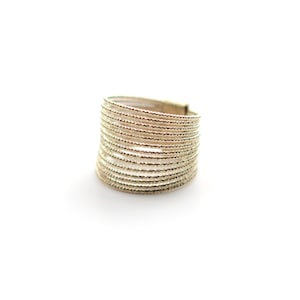 May include: A gold-toned ring with multiple thin bands stacked on top of each other. The bands are textured with a small, raised pattern.