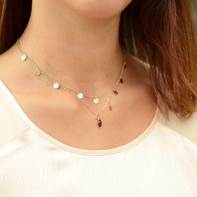 May include: A gold necklace with a red gemstone pendant and a layered chain with small gold circles.