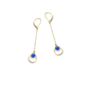 K&ouml;nnte beinhalten: Ein Paar goldene Ohrringe mit blauen Edelstein-Tropfen. Die Ohrringe haben eine zarte Kette und einen tropfenf&ouml;rmigen Rahmen.