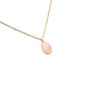 May include: A delicate gold chain necklace with a pale pink oval pendant.