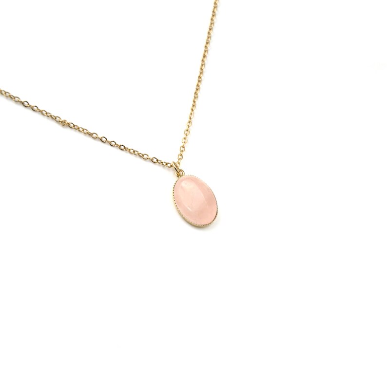 May include: A delicate gold chain necklace with a pale pink oval pendant.