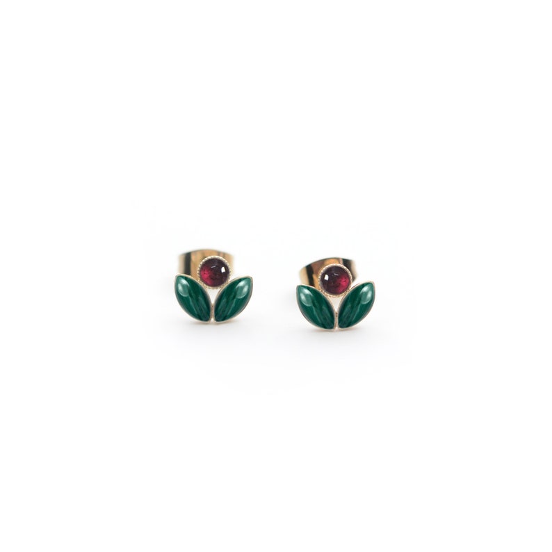May include: A pair of gold earrings with a red gemstone and green enamel leaves.