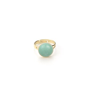 May include: A gold-toned adjustable ring featuring a large, round, pale green stone. The stone is set in a gold bezel with a beaded edge. The ring's band is simple and adjustable.