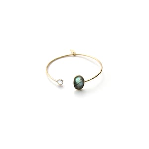 May include: A gold bangle bracelet with a large oval-shaped labradorite gemstone and a smaller round white gemstone.