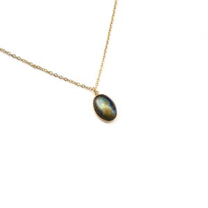 May include: A gold chain necklace with a silver oval pendant featuring a dark blue and green gemstone.