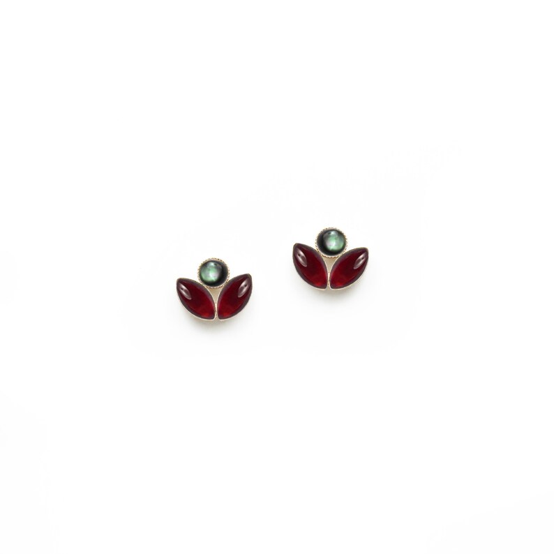May include: A pair of gold earrings with red and green gemstone accents. The earrings are shaped like a flower with three petals.