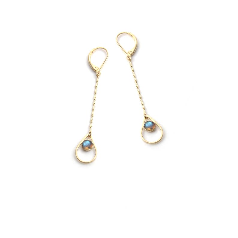 K&ouml;nnte beinhalten: Ein Paar goldene Ohrringe mit einem tropfenf&ouml;rmigen Design und einem blauen Edelstein in der Mitte jedes Tropfens.