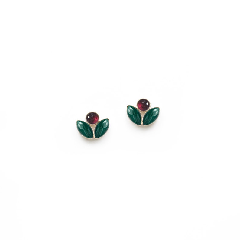 May include: A pair of gold earrings with green and red enamel. Each earring features two green leaves and a red centre.