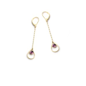 K&ouml;nnte beinhalten: Ein Paar goldene Ohrringe mit einem tropfenf&ouml;rmigen Anh&auml;nger und einem kleinen violetten Edelstein in der Mitte.