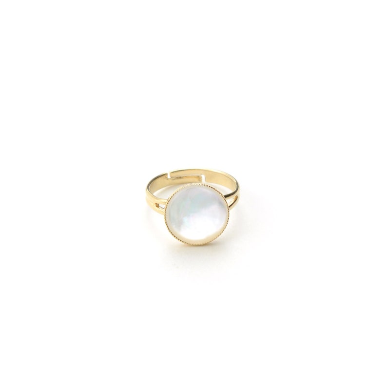 May include: A gold-toned adjustable ring featuring a large, round, iridescent mother-of-pearl center stone. The ring has a simple, elegant design, with a thin band and a decorative edge around the stone.