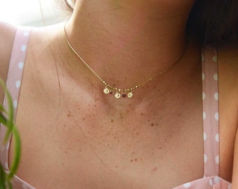 Può includere: Una collana a catena d'oro con piccoli ciondoli rotondi d'oro e pietre preziose rosse.