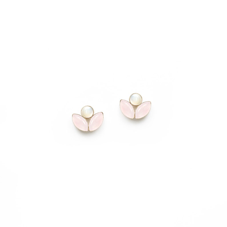 May include: A pair of gold earrings with pink and white gemstone accents. The earrings are shaped like a flower with three petals.