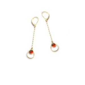 K&ouml;nnte beinhalten: Ein Paar goldene Ohrringe mit einem tropfenf&ouml;rmigen Design und einem kleinen roten Edelstein in der Mitte jedes Tropfens.