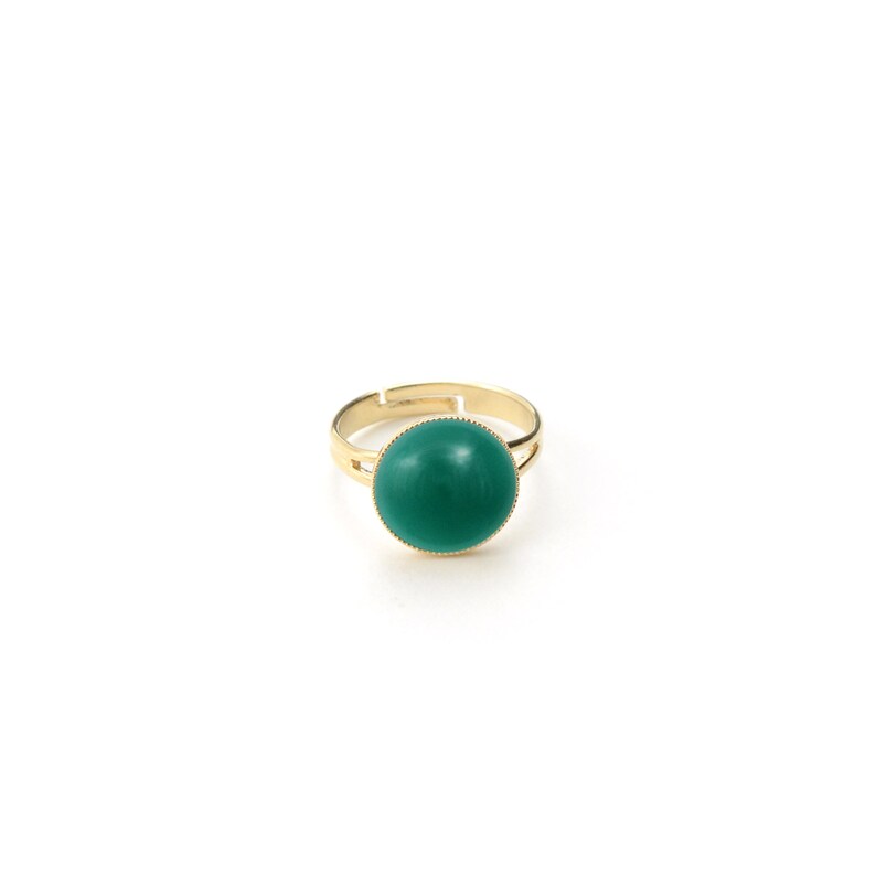 May include: A gold-toned adjustable ring featuring a large, round, teal-colored stone. The ring's band is thin and smooth, with a simple design. The teal stone is the focal point, set in a gold bezel.