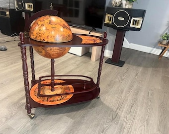 May include: A dark wood globe bar cart featuring a spherical world globe that opens to reveal storage space. The cart has a top shelf, a lower shelf with a decorative compass rose design, four turned legs, and small metal casters for mobility.